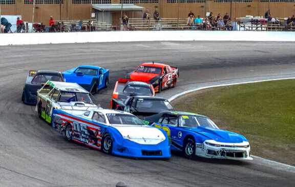 Stock cars racing side by side through a turn at Auburndale Speedway